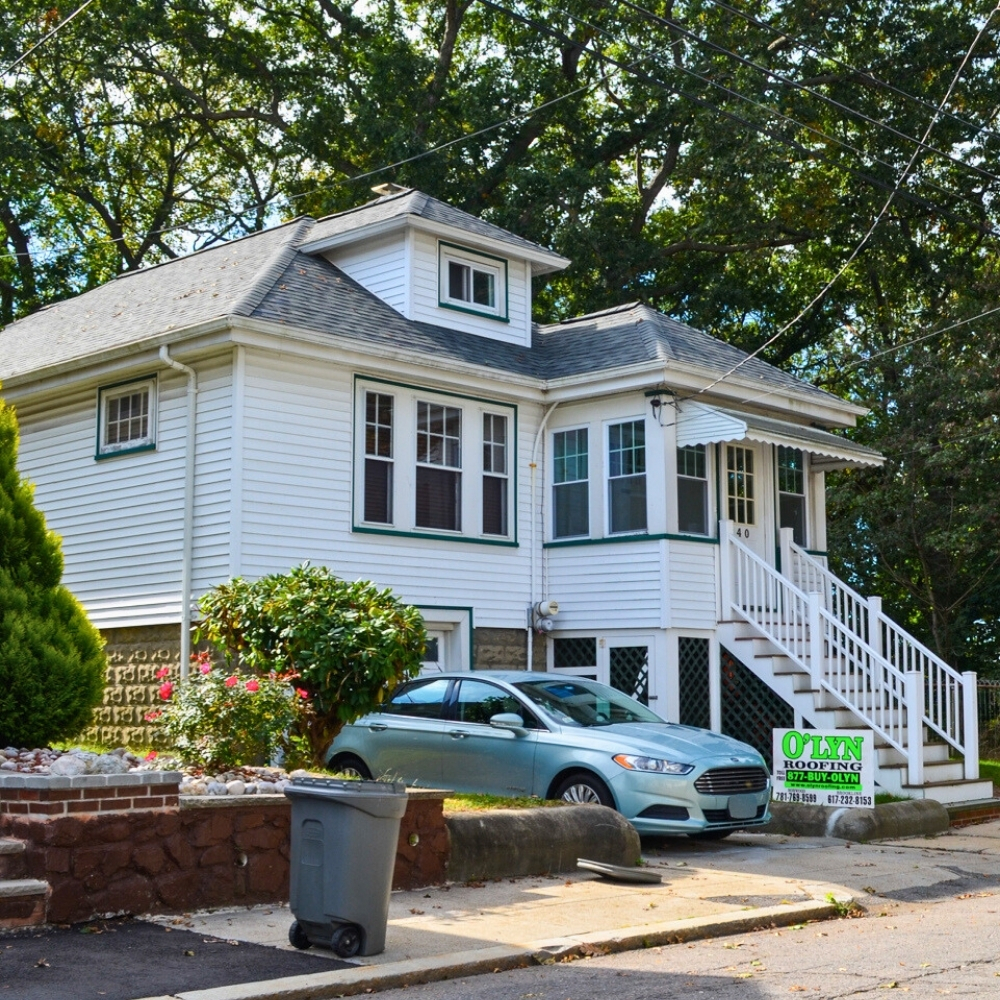 New roof on a small house with white siding. Car in driveway. Trees in background.