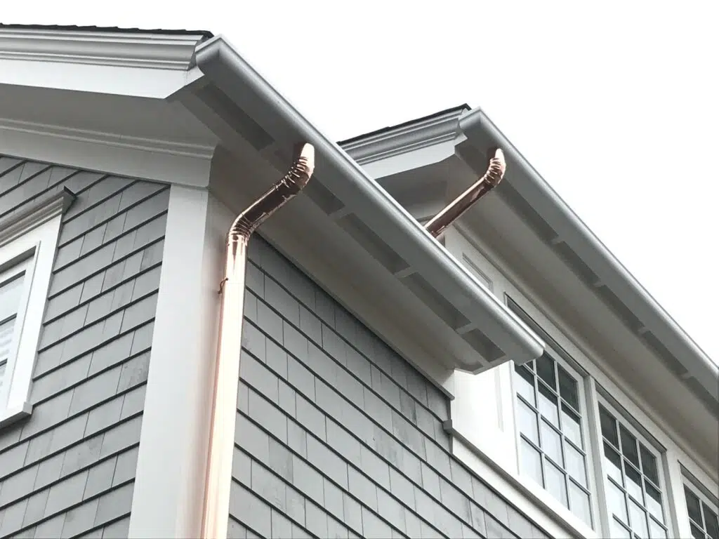 Fiberglass gutters with copper downspout drain installed on a two-story light gray home.